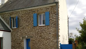 Ein Haus aus Stein mit einer blauen Tür und Fensterläden, einer Schotterauffahrt und einem Holzzaun.