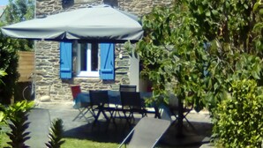 Ein Steinhäuschen mit überdachter Terrasse, Gartenmöbeln und üppigem Garten.