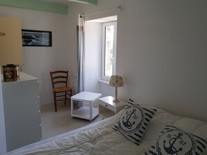A bedroom with a bed, a chair, a small table, a lamp, and a window.