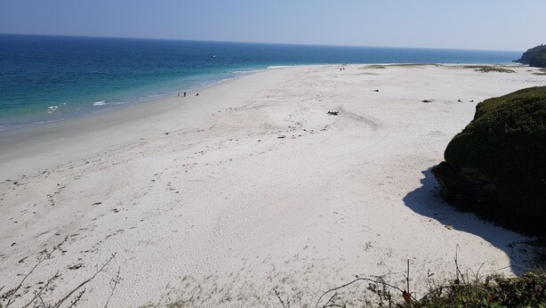 Ein weiter Sandstrand mit klarem, blauem Wasser und einem Felsen im rechten Bildrand.