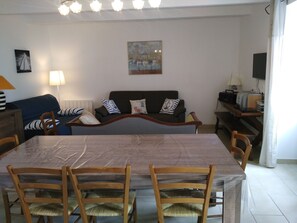A living room with a sofa, a dining table with chairs, a lamp, and a painting on the wall.