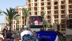 A hotel courtyard with outdoor seating, palm trees, and a large screen displaying a sports event. - house / villa - SOUSSE (Sousse)