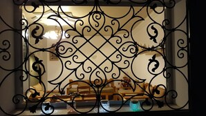 A view through a decorative metal gate with a lattice design, leading to a room with a wooden bench, a table, and a vase with flowers. - house / villa - SOUSSE (Sousse)