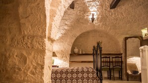 A rustic stone-walled room with a patterned bed, wooden chairs, and a small table. - Magnificent Villa in Alberobello with Trulli and exclusive salt water swimming pool (Alberobello)