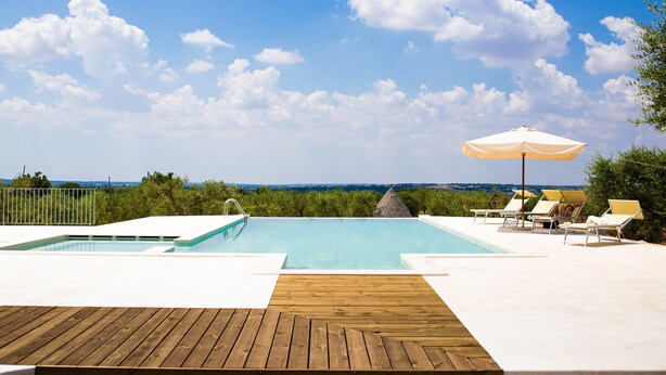 A pool with a wooden deck, lounge chairs, and an umbrella. - Magnificent Villa in Alberobello with Trulli and exclusive salt water swimming pool (Alberobello)