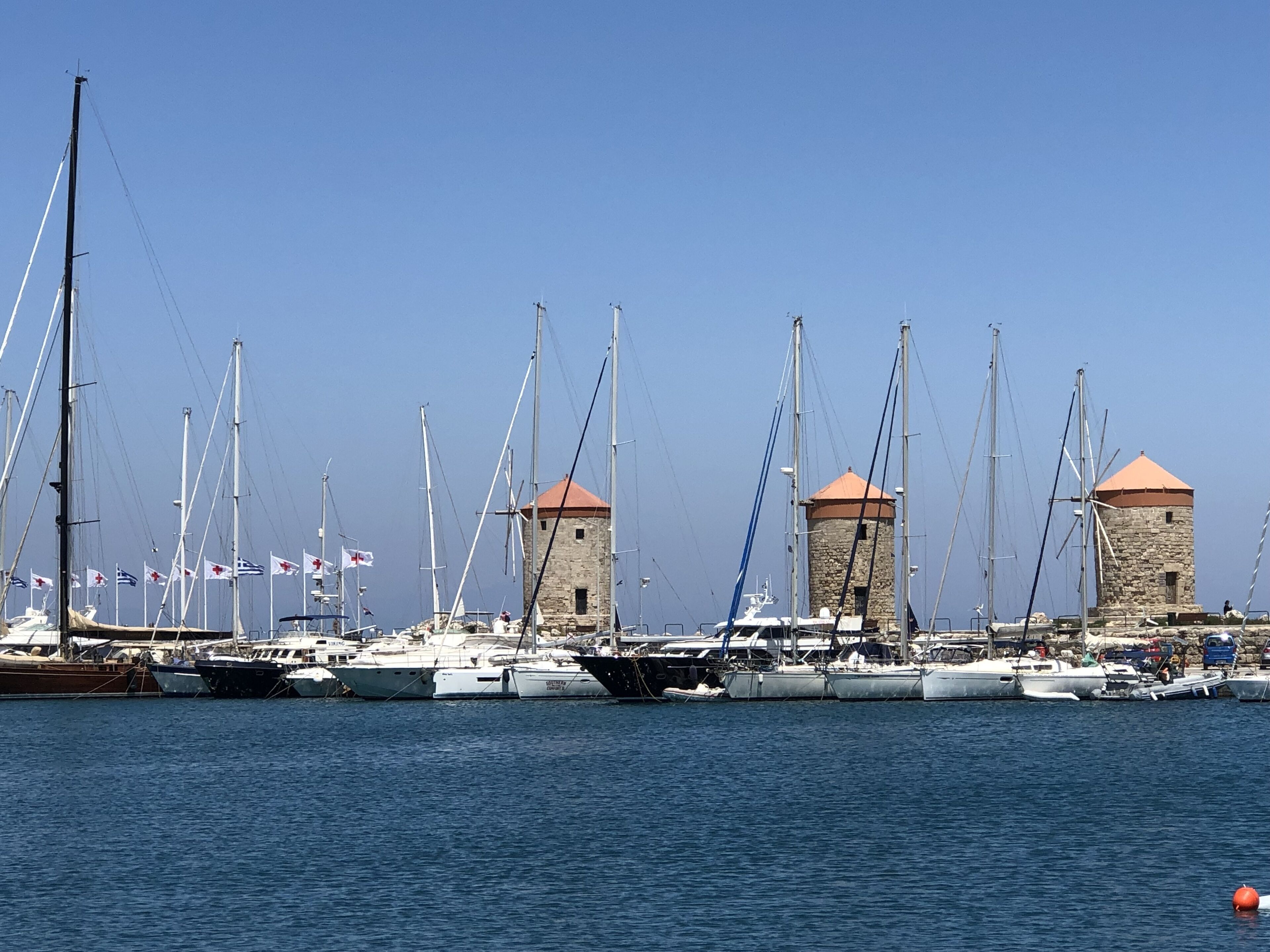 Een jachthaven met verschillende zeilboten afgemeerd, stenen torens en vlaggen.