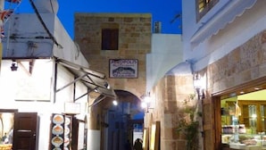 Un vicolo stretto con edifici in pietra, insegna di un ristorante e bandiere.