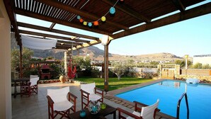 Una terrazza esterna con piscina, mobili in legno e vista sulle montagne.