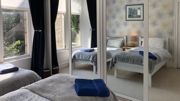 A bedroom with two beds, a large window with curtains, a mirror, and a floral wallpaper. - Apartment To Suit All! Perfect Location With Easy Access To Centre Of Town (Aberdeen)