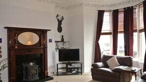 A living room with a fireplace, a television on a stand, a sofa, and a window with curtains. - Apartment To Suit All! Perfect Location With Easy Access To Centre Of Town (Aberdeen)