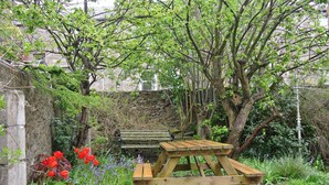 A wooden picnic table in a garden with a stone wall, flowering plants, and trees. - Apartment To Suit All! Perfect Location With Easy Access To Centre Of Town (Aberdeen)