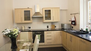 A modern kitchen with wooden cabinets, a glass dining table, and a vase of flowers. - Apartment To Suit All! Perfect Location With Easy Access To Centre Of Town (Aberdeen)