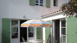 En terrasse med et bord og stole, en stribet parasol og grønne skodder.