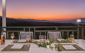 A table set for two with wine glasses, a candle, and a bottle of rosé wine, overlooking a sunset view.