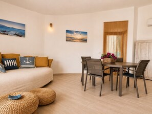Een kamer met een bed, een eettafel met stoelen, een raam met gordijnen en kunstwerken aan de muur.