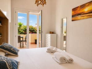 A bedroom with a bed, a dresser, a mirror, and a view of a balcony with plants.