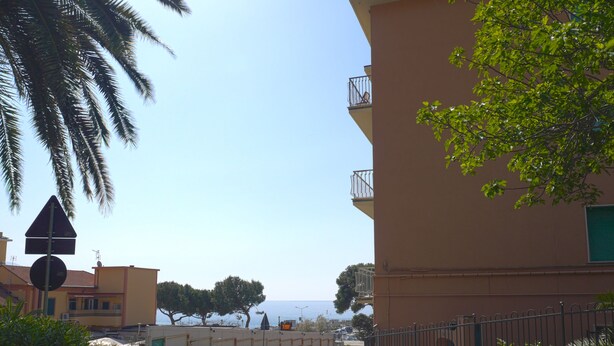 A curved road with a stone wall and a metal fence on one side, and a building with balconies on the other. - BLUE DIAMOND in the 5Terre-Cod. Citra 011019-LT-0241 (Monterosso al Mare)