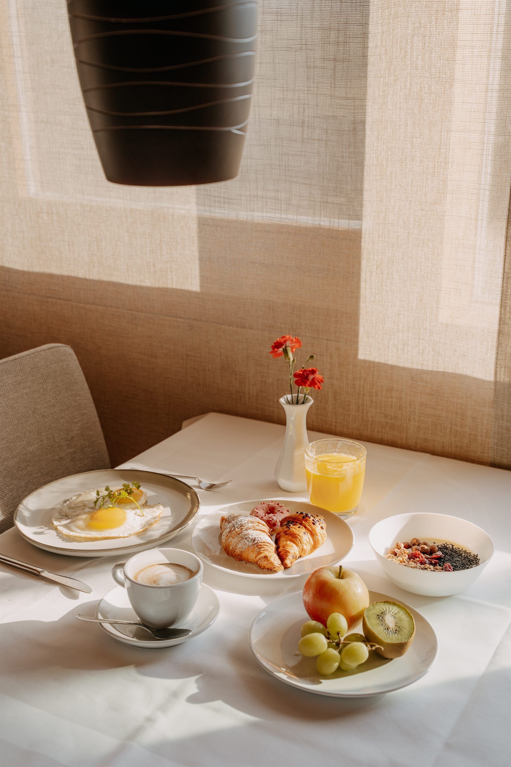 A breakfast setting with plates of food, a cup of coffee, a glass of orange juice, and a vase with flowers.
