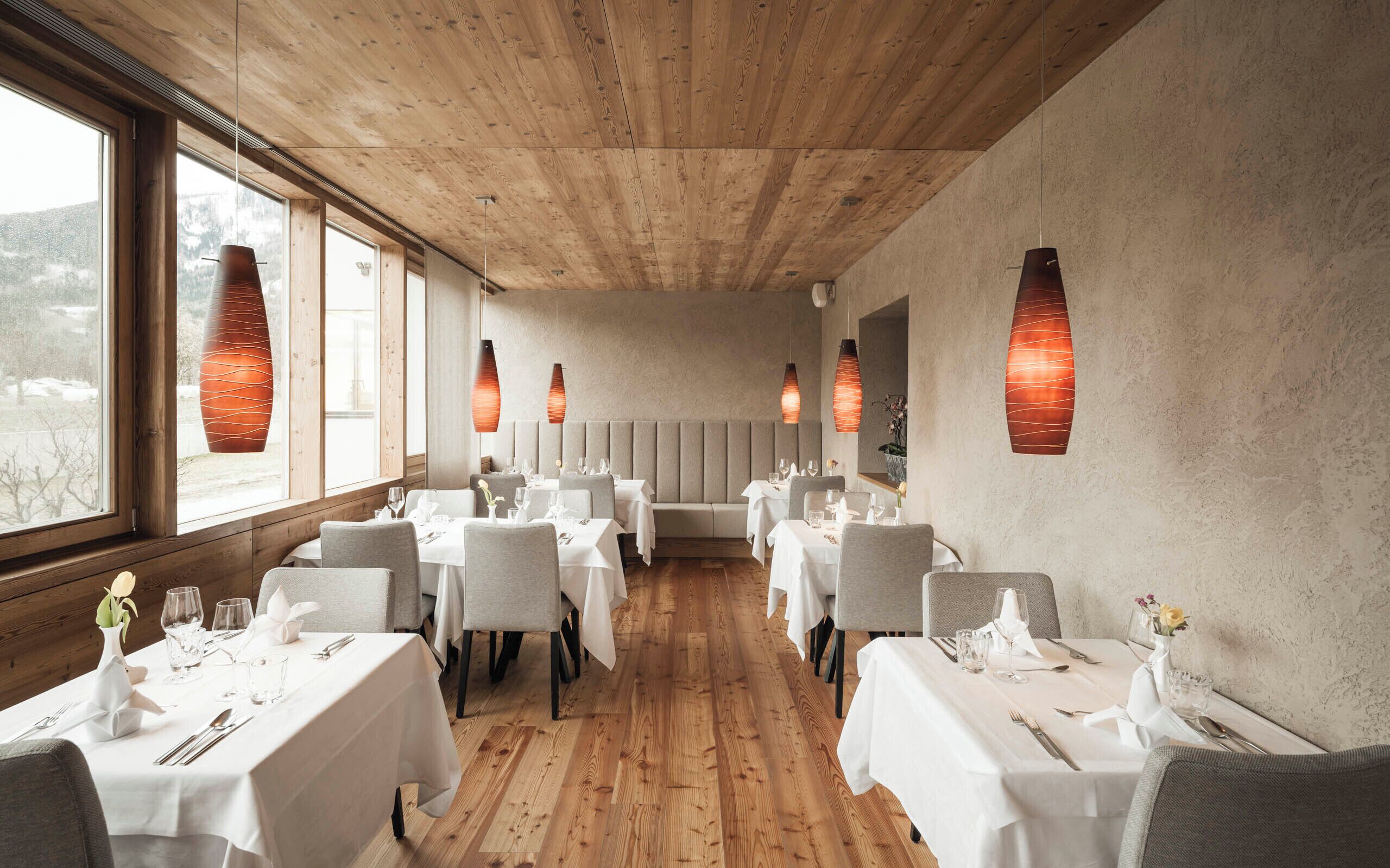 A restaurant with wooden ceiling and walls, white tables, and hanging pendant lights.