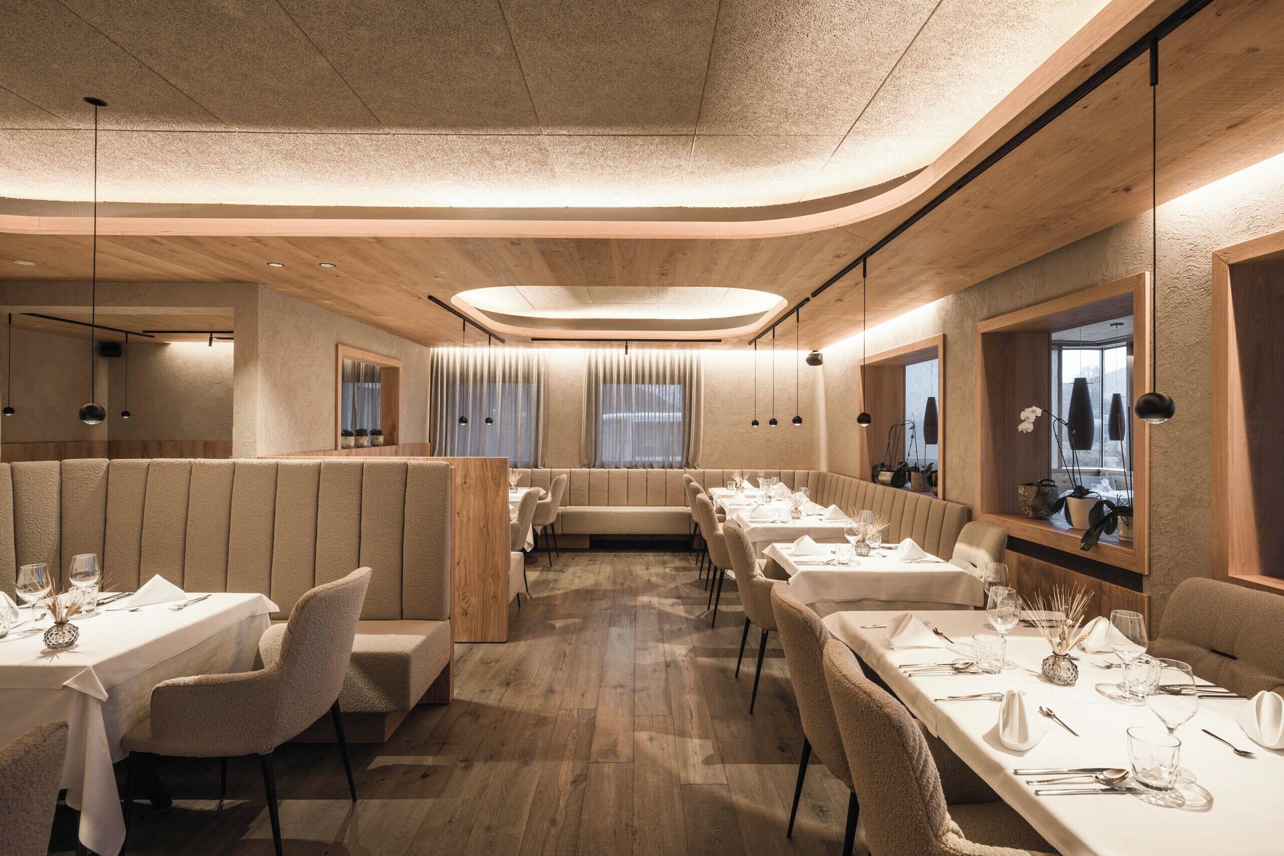 Ein Restaurant mit Holzwänden, langen Tischen und Sitzgruppen.