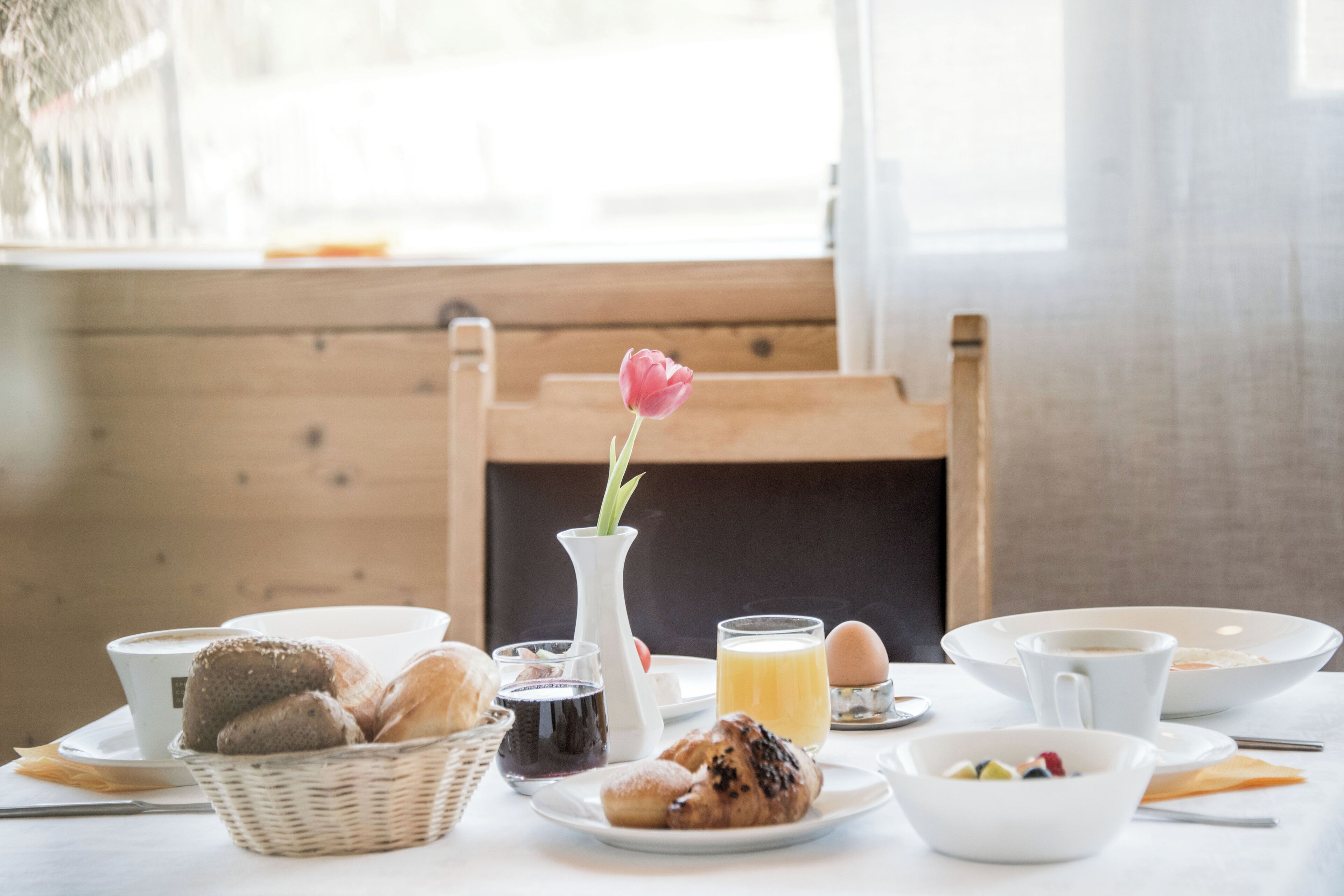 Una mesa de desayuno con pan, pastelería, un florero con una flor y una taza de café.
