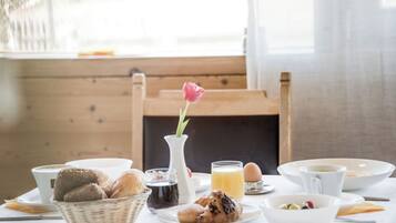 Una mesa de desayuno con pan, pastelería, un florero con una flor y una taza de café.