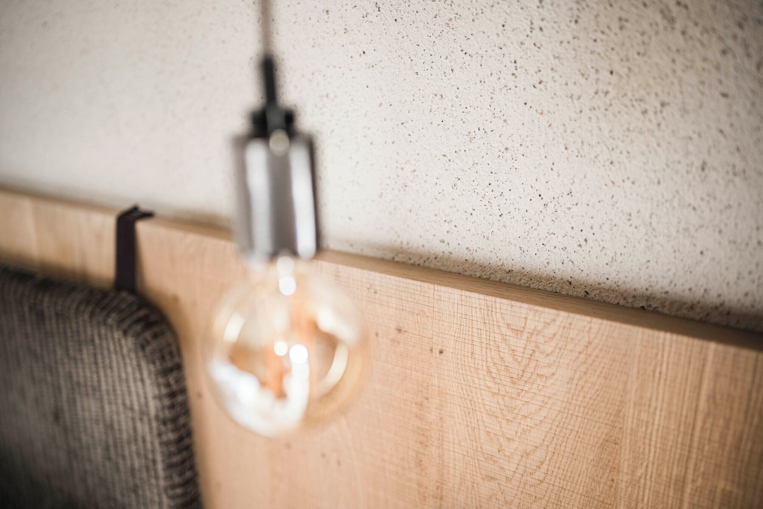 A close-up of a light bulb hanging from a ceiling, a wooden surface below, and a textured wall.