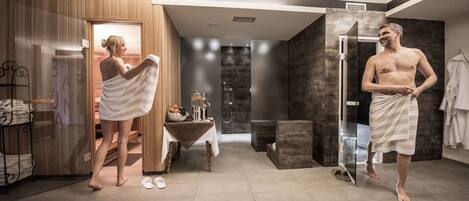 A modern bathroom with a wooden sauna, a glass shower enclosure, and a table with toiletries.