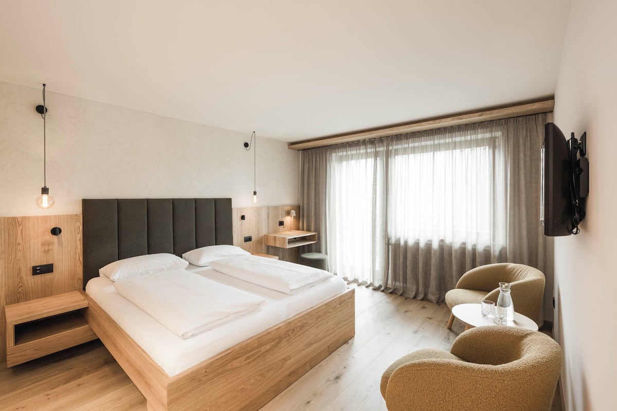 Een moderne hotelkamer met een houten bed, een klein bureau, een stoel en een aan de muur bevestigde televisie.