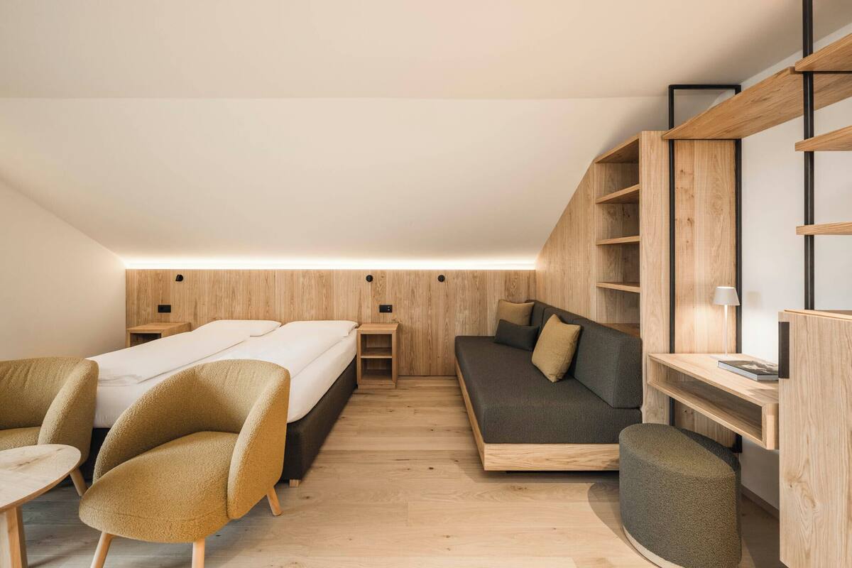 Een compacte, moderne kamer met een bed, een slaapbank en een zithoek, met houten wanden en een ingebouwde plank.