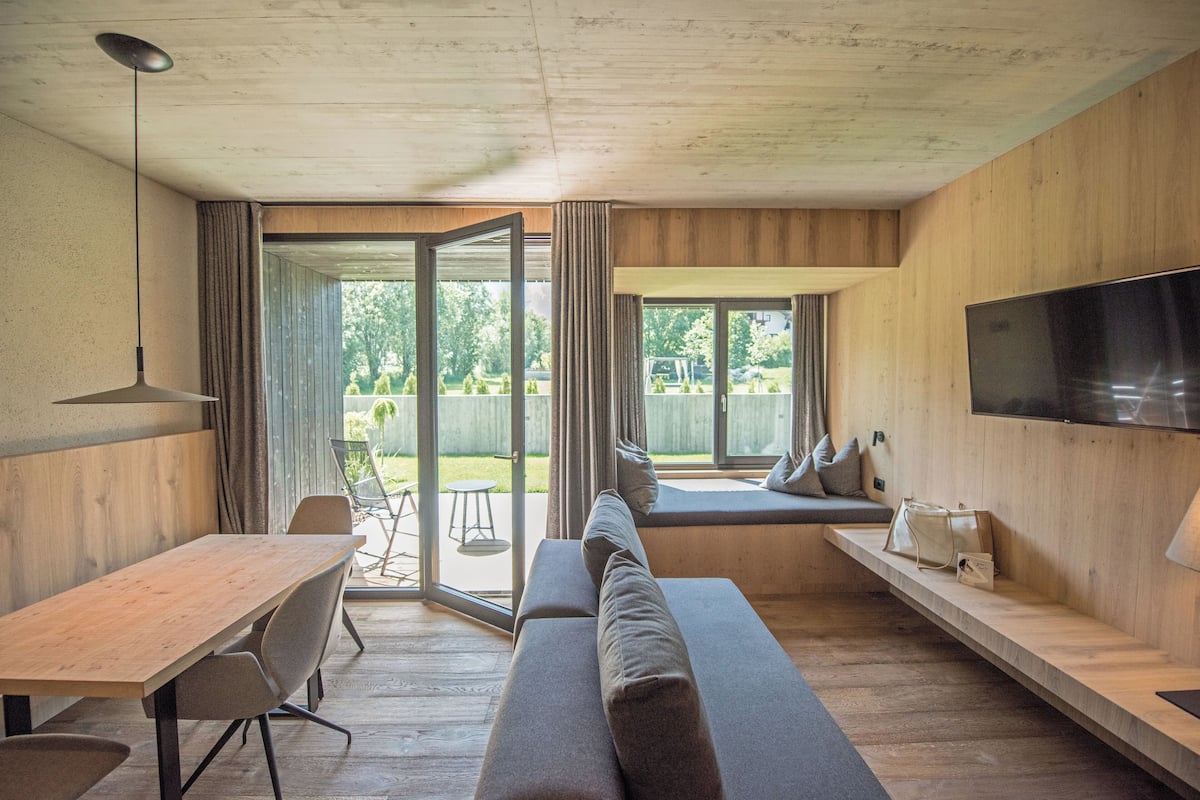 Een moderne woonkamer met een houten vloer, een bank, een eettafel en een aan de muur bevestigde televisie.