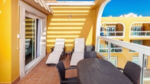 A balcony with a table and chairs, a sliding glass door, and a yellow wall.