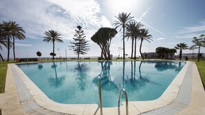 A swimming pool with clear blue water, surrounded by palm trees and a grassy area. - DELUXE APARTMENT- BEACHFRONT, SWIMMING POOL, A/A, FREE WIFI AND PARKING (Torremolinos)