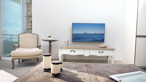 A room with a wooden coffee table, a chair, a small table with a bowl, and a painting of the ocean on the wall. - DELUXE APARTMENT- BEACHFRONT, SWIMMING POOL, A/A, FREE WIFI AND PARKING (Torremolinos)