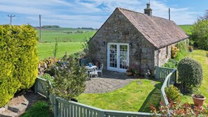 A stone cottage with a tiled roof, a patio with outdoor furniture, and a well-maintained garden. - Beautiful, detatched 300 year old, fully renovated cottage with country views (Perth & Kinross)