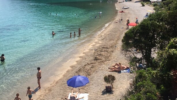 A beach with clear turquoise water, people swimming and sunbathing, and a rocky cliff in the background. - 3 bedroom villa, sea 5 minutes walk, private parking & garden, quiet location (Ulica Bana  Mazuranica)