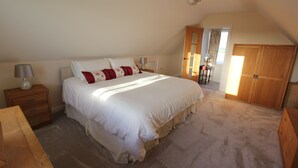 Quarto com uma cama grande, um guarda-roupa de madeira, uma mesa de cabeceira e uma escrivaninha.