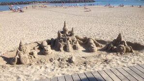 Une plage de sable avec une promenade en bois qui mène à un espace aménagé pour construire des châteaux de sable.