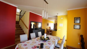 A dining area with a table set for four, a staircase, and a kitchen in the background. - Breathtaking Views Holiday House with Heat and or Air conditioning System (Arco da Calheta)