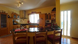 A spacious kitchen with wooden cabinets, a central island, and a dining area with chairs. - Breathtaking Views Holiday House with Heat and or Air conditioning System (Arco da Calheta)
