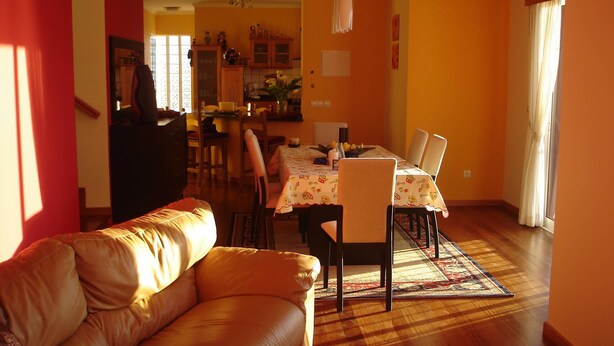 Un salon avec un canapé en cuir, un coin repas avec une table dressée pour quatre personnes, et une cuisine en arrière-plan.