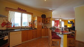 A kitchen with wooden cabinets, a dining area with a red table, and a view of the outdoors through the window. - Breathtaking Views Holiday House with Heat and or Air conditioning System (Arco da Calheta)
