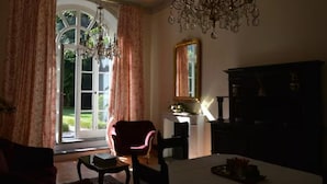 A room with a large window, a chandelier, a mirror, and a dark wooden cabinet. - Apartment with private Italian-style garden, a few steps from the lake. (Bellagio)