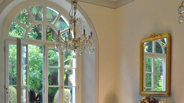 A room with a large arched window, a chandelier, a mirror, and a fireplace. - Apartment with private Italian-style garden, a few steps from the lake. (Bellagio)