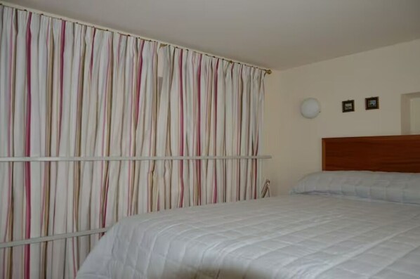 A bedroom with a bed, a curtain, a wooden headboard, and a wall-mounted light fixture.