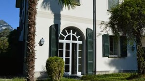 A white building with green shutters, a central arched window, and a small entrance. - Apartment with private Italian-style garden, a few steps from the lake. (Bellagio)