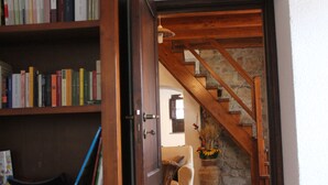 Una escalera de madera con paredes de piedra, una estantería llena de libros y un sillón con un jarrón de flores.