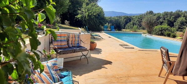 Area piscina con lettini e divano, circondata dal verde e con vista sulle montagne.