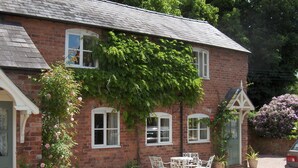 A brick house with a gravel driveway, white outdoor furniture, and potted plants.