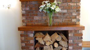A brick fireplace with a wooden mantel and a vase of white flowers.
